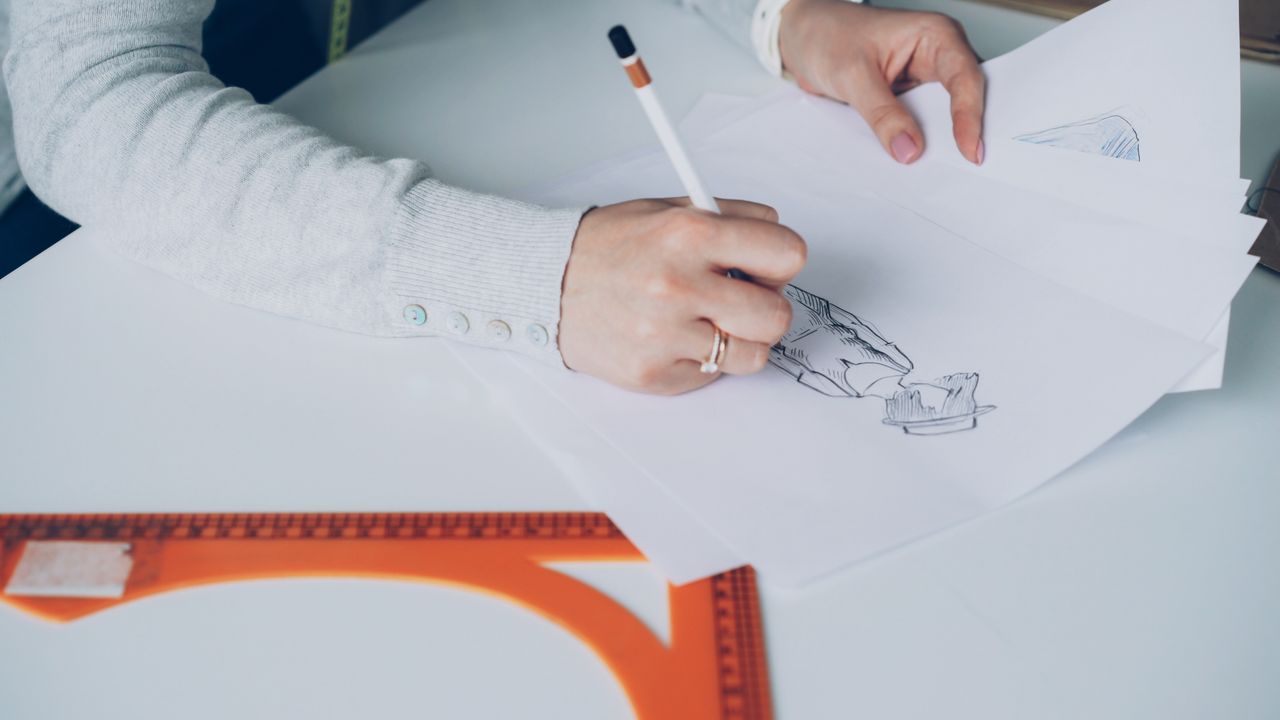 Close-up of an artist designing fashion sketches while seated at a desk indoors.